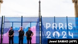 Ofițeri ai Jandarmeriei franceze stau de pază în fața unui gard de securitate decorat cu un banner al Jocurilor Olimpice Paris 2024 pe esplanada Trocadero, lângă Turnul Eiffel din Paris, înaintea Jocurilor Olimpice de la Paris, 9 iulie 2024.