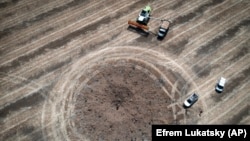 Un fermier adună recolta în jurul unui crater lăsat de o rachetă rusească în regiunea Dnipropetrovsk, Ucraina, în iulie 2022.