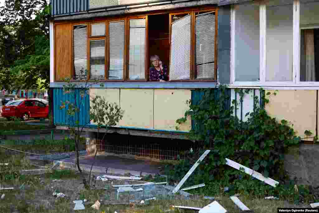 O femeie al cărei apartament a fost avariat în timpul atacului vorbește la telefon în timp ce echipele de intervenție de urgență lucrează în apropiere. 