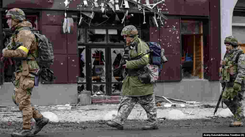 Militari trecând pe lângă o cafenea în ruine din Bahmut. Dubceak spune că obuzele cad necontenit, „e chiar o nebunie” în centrul orașului, pentru că „Rusia bombardează fără nici o noimă”. „Se aud explozii la fiecare minut”.