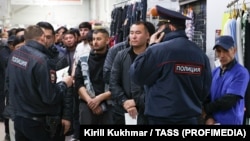 Muncitori migranți așteaptă verificarea documentelor în timpul unei percheziții la un centru comercial din Novosibirsk, Rusia, pe 15 octombrie.
