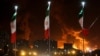 Iran - Iranian flags fly as fire and smoke from an Israeli attack on Sharan Oil depot rise, following Israeli strikes on Iran, in Tehran, June 15, 2025.